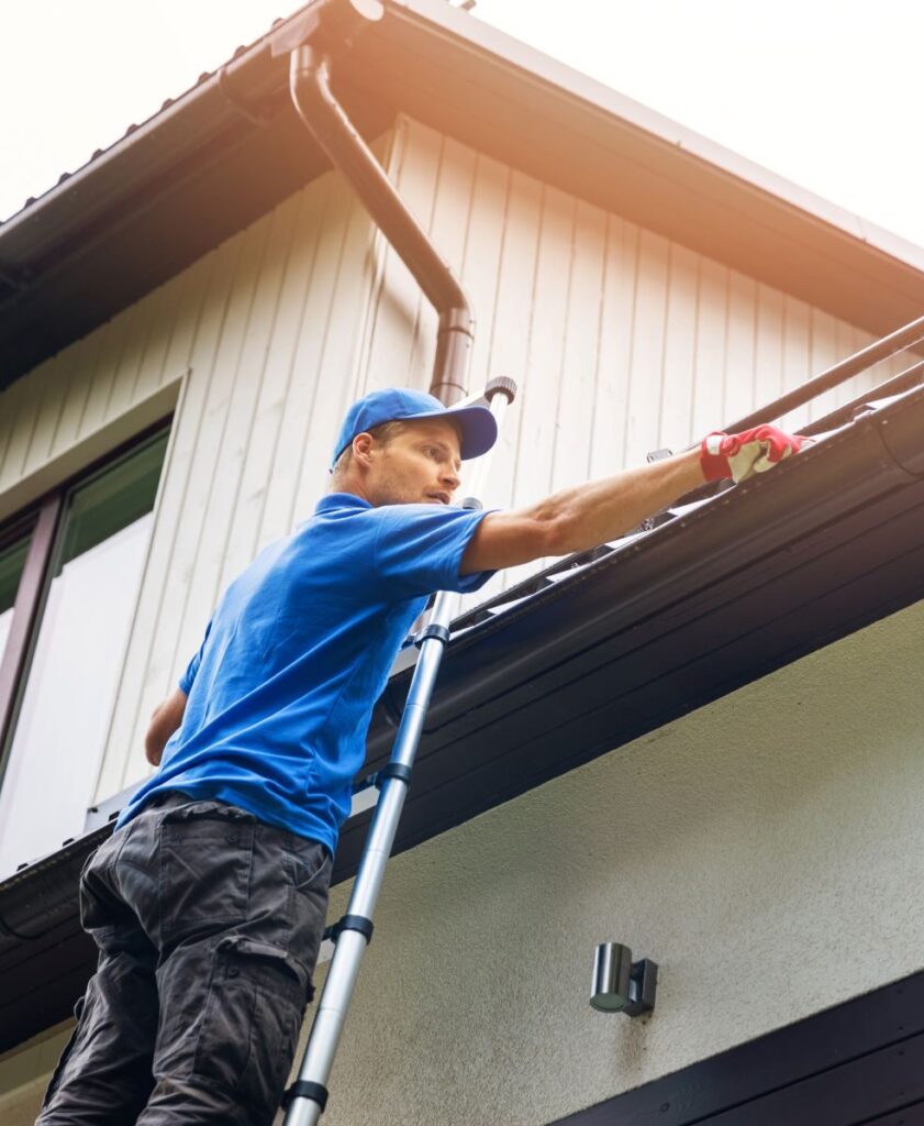 A man on a ladder cleaning the roof of a house.