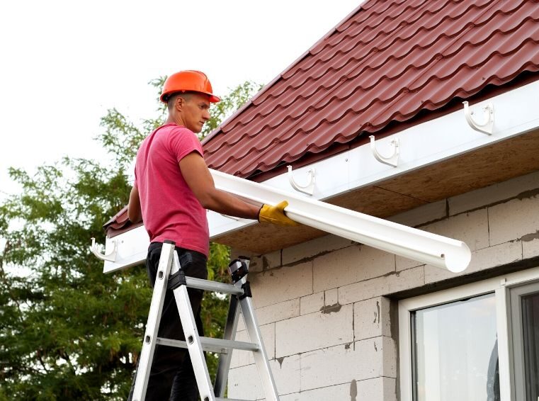 A man on a ladder cleaning the roof of a house.